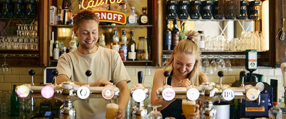 Barpersoneel tapt biertjes onder het Smirnoff-bord